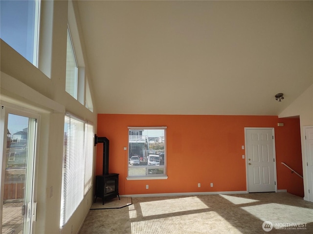 unfurnished living room with a wood stove, high vaulted ceiling, carpet floors, and baseboards