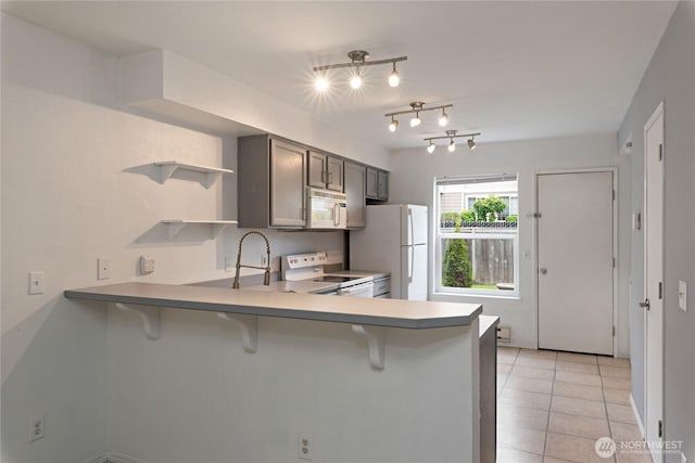 9817 132nd Street Ct E Unit B, Puyallup, WA 98373 - kitchen with white appliances, a kitchen breakfast bar, a peninsula, open shelves, and light tile patterned flooring