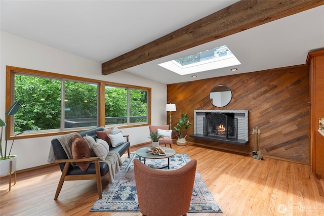 living area featuring a skylight, a fireplace, wooden walls, light wood-style floors, and beam ceiling