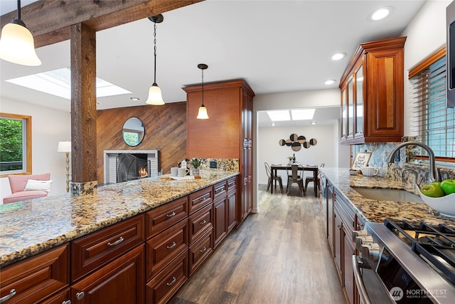 kitchen featuring stainless steel gas stove, a sink, dark wood-style floors, light stone countertops, and a fireplace