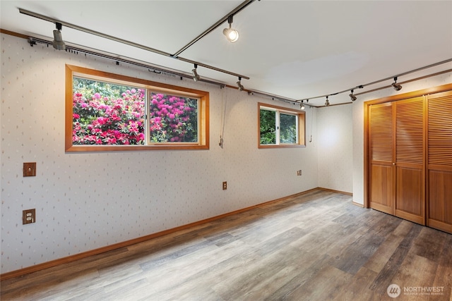 basement with rail lighting, wood finished floors, and wallpapered walls