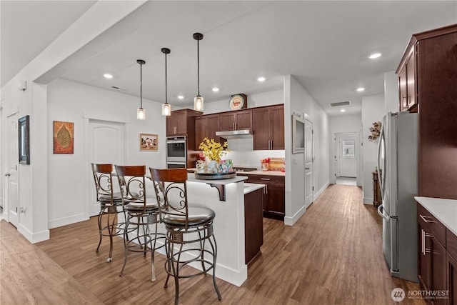 179 N Shore Dr, Orondo, WA 98843 - kitchen with stainless steel appliances, under cabinet range hood, a kitchen bar, a center island, and wood finished floors