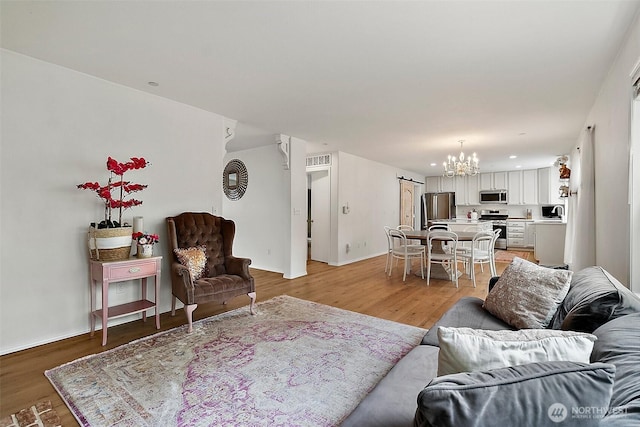 living area with a chandelier, light wood finished floors, a barn door, and baseboards
