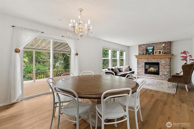 dining space with light wood finished floors, a chandelier, and a brick fireplace