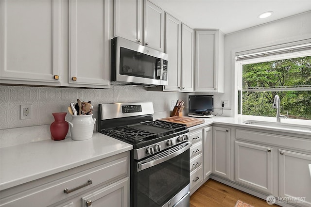 kitchen featuring appliances with stainless steel finishes, a sink, backsplash, light countertops, and recessed lighting