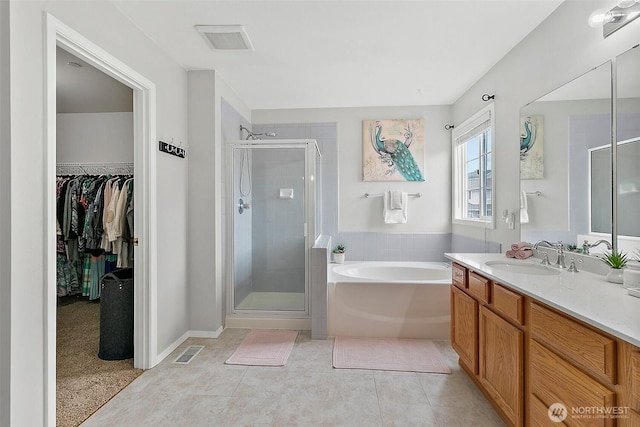 bathroom with a stall shower, vanity, a garden tub, a walk in closet, and tile patterned floors