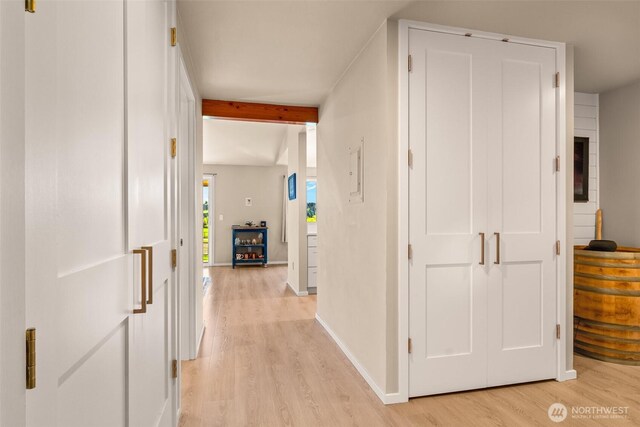 hallway with light wood-type flooring, baseboards, and beam ceiling