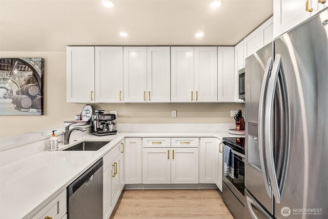 kitchen featuring stainless steel appliances, white cabinets, a sink, light countertops, and light wood-style floors