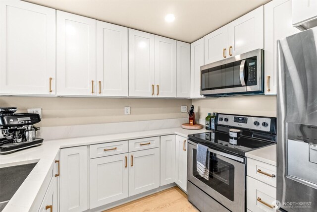 kitchen featuring appliances with stainless steel finishes, white cabinetry, light countertops, light wood-style floors, and a sink