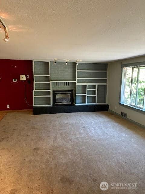 816 Sunrise Ln, Centralia, WA 98531 - unfurnished living room with track lighting, a textured ceiling, carpet floors, a fireplace, and baseboards