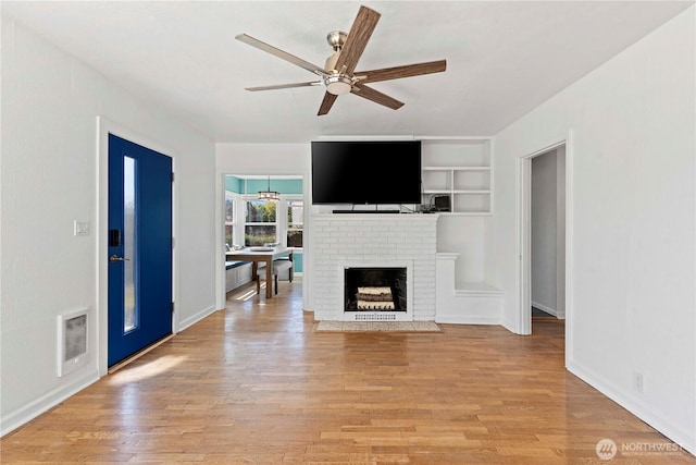 unfurnished living room featuring ceiling fan, light wood finished floors, built in shelves, and a fireplace
