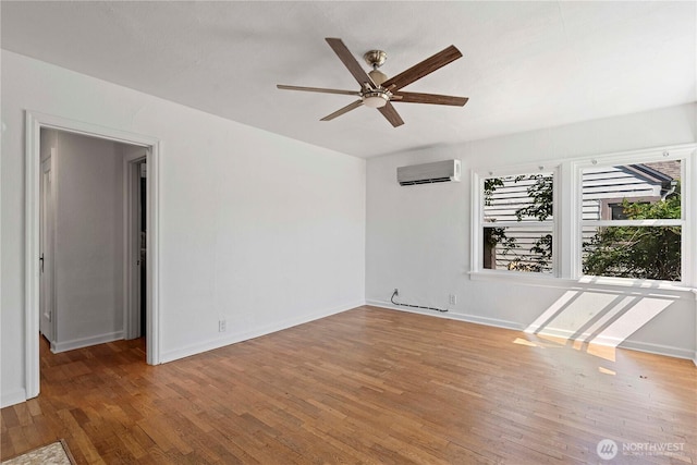 spare room featuring a wall mounted air conditioner, ceiling fan, wood finished floors, and baseboards