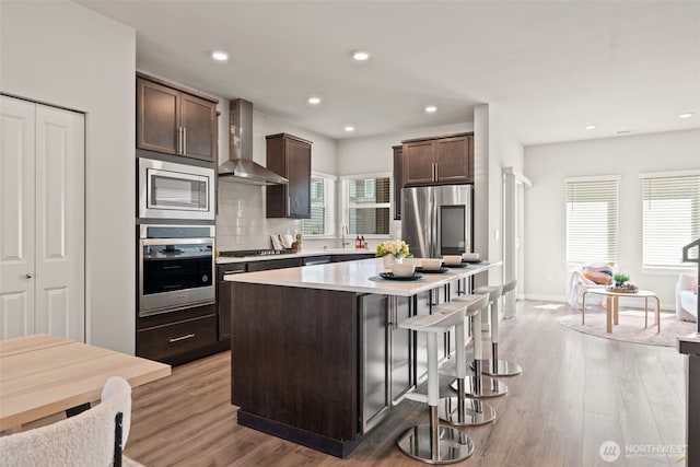 207 207th St SE Unit Eh49, Bothell, WA 98012 - kitchen featuring wall chimney exhaust hood, stainless steel appliances, a sink, dark brown cabinets, and light wood-style floors