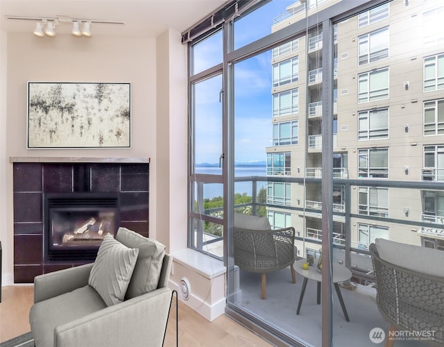 sitting room with rail lighting, a water view, a wall of windows, a tile fireplace, and wood finished floors