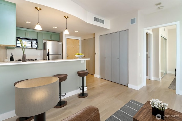 kitchen with green cabinets, freestanding refrigerator, light wood-style floors, a peninsula, and recessed lighting