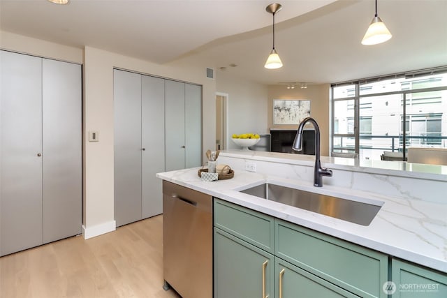 kitchen featuring green cabinets, a sink, light wood-style floors, pendant lighting, and light stone countertops