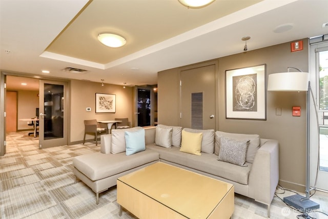 living area featuring baseboards, light carpet, and a raised ceiling