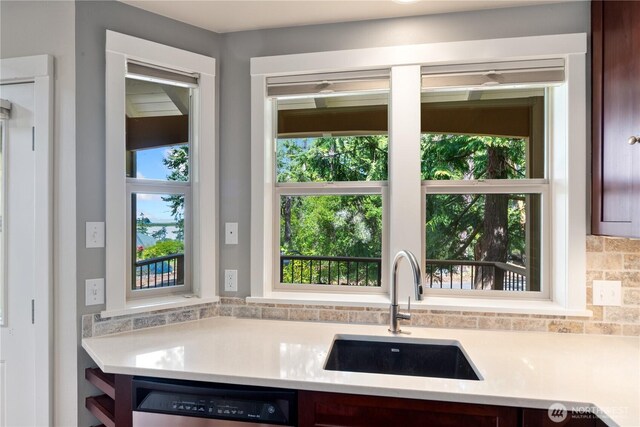 kitchen featuring stainless steel dishwasher, light countertops, a sink, and decorative backsplash
