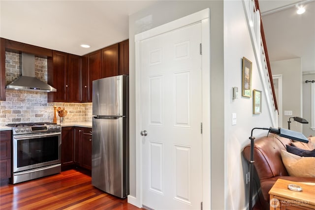 kitchen with stainless steel appliances, wall chimney range hood, light countertops, dark wood finished floors, and decorative backsplash