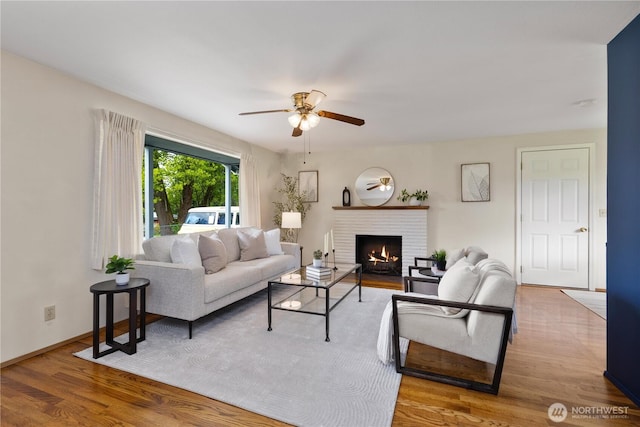 living area with ceiling fan, a brick fireplace, wood finished floors, and baseboards