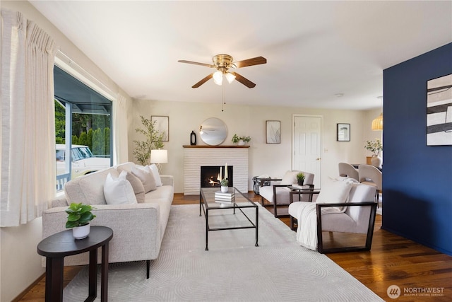 living area with a ceiling fan, wood finished floors, and a brick fireplace