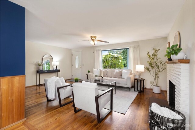living area with a ceiling fan, wood finished floors, and a brick fireplace