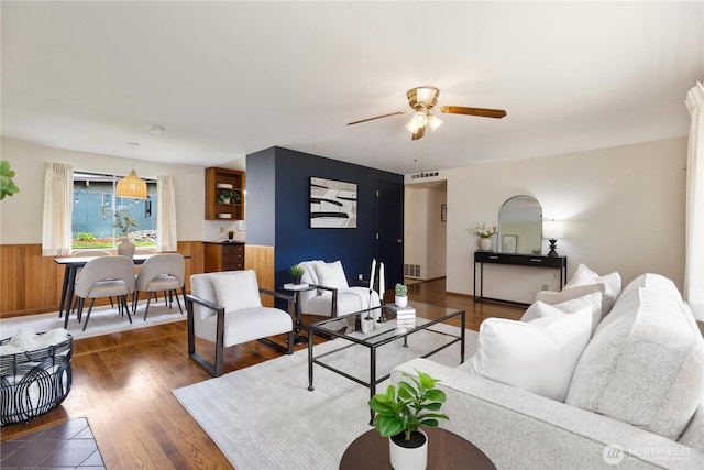 living room featuring a ceiling fan, wainscoting, and dark wood finished floors