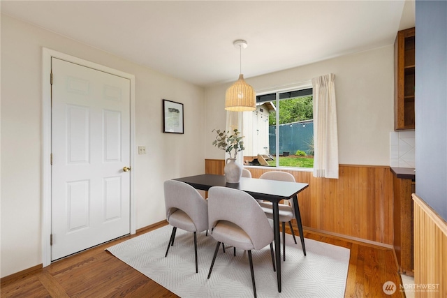 dining space with a wainscoted wall, wood finished floors, and wooden walls