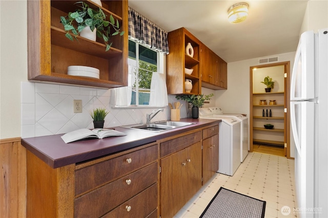 kitchen with freestanding refrigerator, open shelves, a sink, washer and dryer, and decorative backsplash