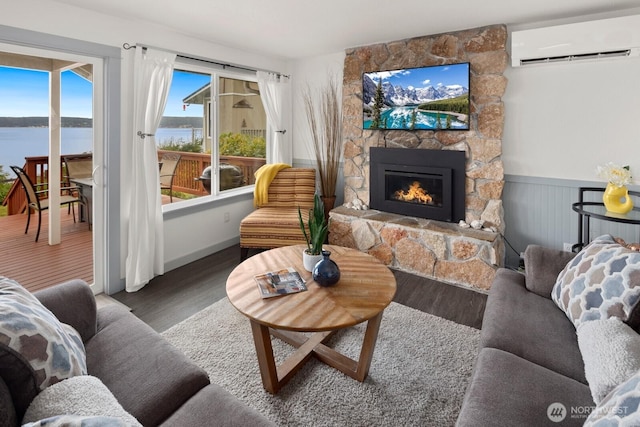 2967 Saratoga Rd, Langley, WA 98260 - living area featuring a wall mounted AC, wood finished floors, a stone fireplace, a water view, and a wainscoted wall