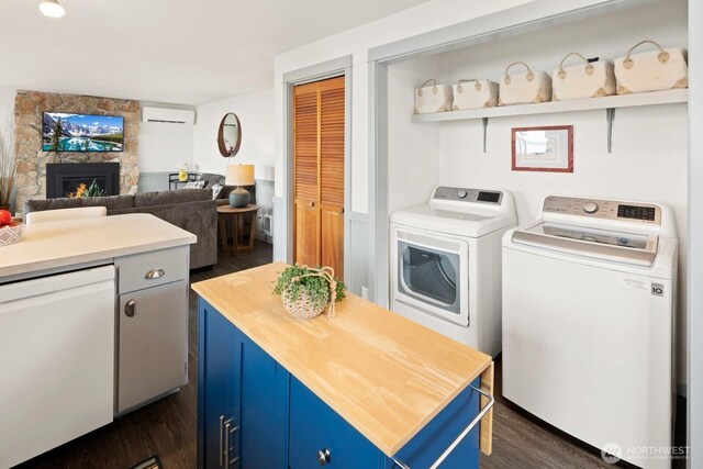 2967 Saratoga Rd, Langley, WA 98260 - laundry area featuring dark wood-style floors, a wall mounted air conditioner, washing machine and clothes dryer, and a stone fireplace