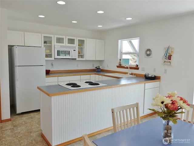 kitchen featuring white appliances, a sink, white cabinetry, glass insert cabinets, and recessed lighting
