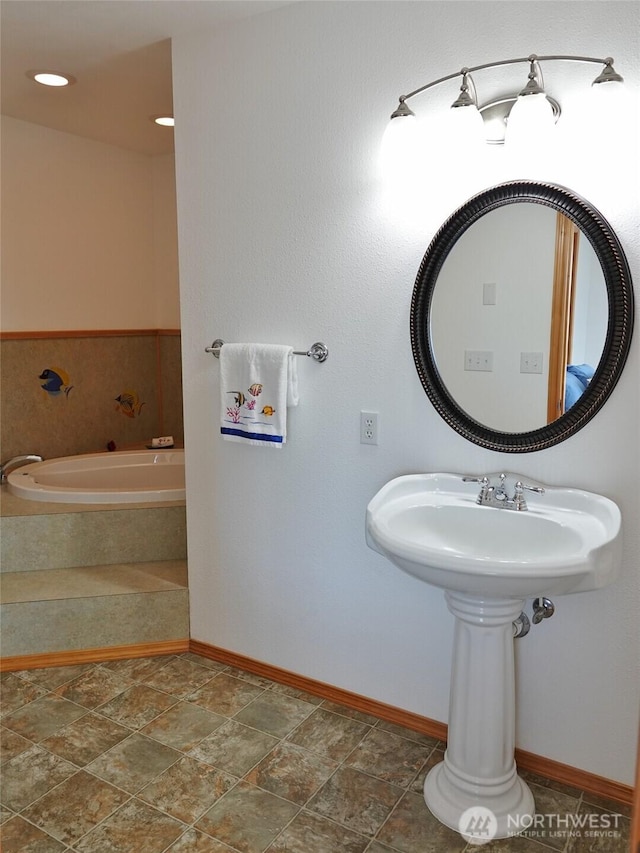 bathroom featuring a relaxing tiled tub, baseboards, and stone finish flooring