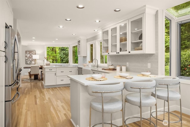 kitchen with a peninsula, freestanding refrigerator, white cabinetry, recessed lighting, and light wood-style flooring