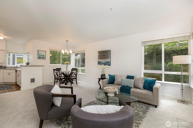 carpeted living room featuring a chandelier, baseboards, and a sink