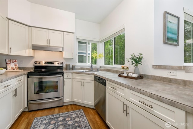 kitchen featuring appliances with stainless steel finishes, under cabinet range hood, a sink, white cabinets, and light wood-type flooring