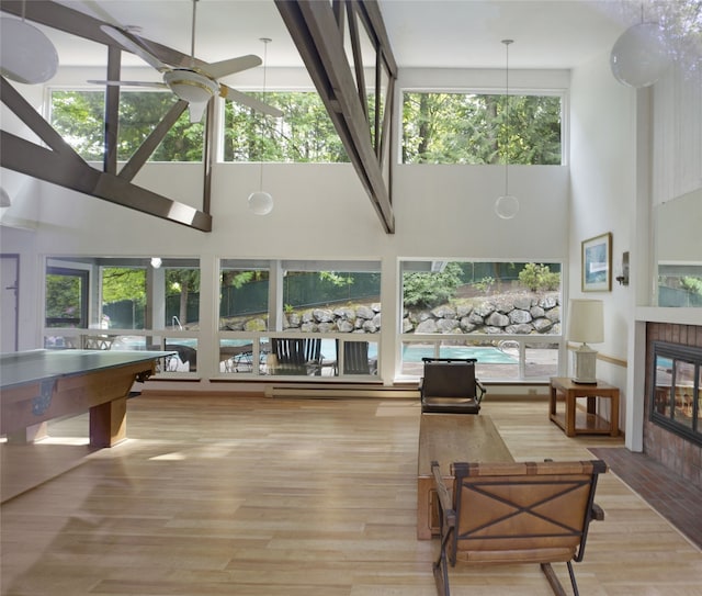 living room with a towering ceiling, a ceiling fan, a fireplace, wood finished floors, and a baseboard heating unit