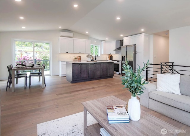 living room featuring a wall unit AC, vaulted ceiling, healthy amount of natural light, light wood-style flooring, and recessed lighting