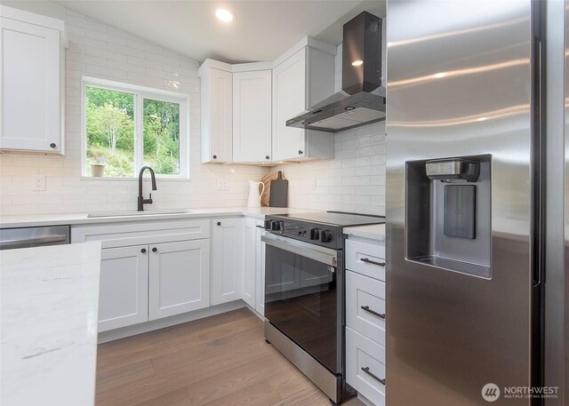 kitchen with stainless steel appliances, wall chimney exhaust hood, a sink, backsplash, and white cabinetry