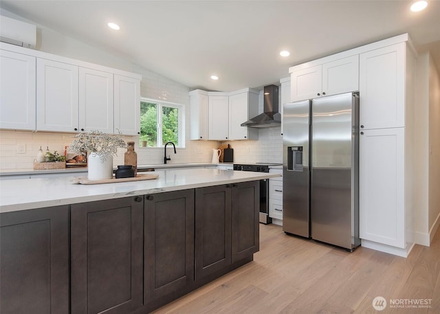 kitchen with appliances with stainless steel finishes, wall chimney exhaust hood, backsplash, white cabinetry, and lofted ceiling