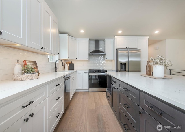 kitchen featuring stainless steel appliances, a sink, wall chimney range hood, white cabinetry, and recessed lighting
