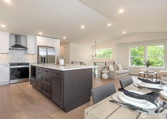 kitchen featuring wall chimney exhaust hood, appliances with stainless steel finishes, light countertops, white cabinets, and lofted ceiling