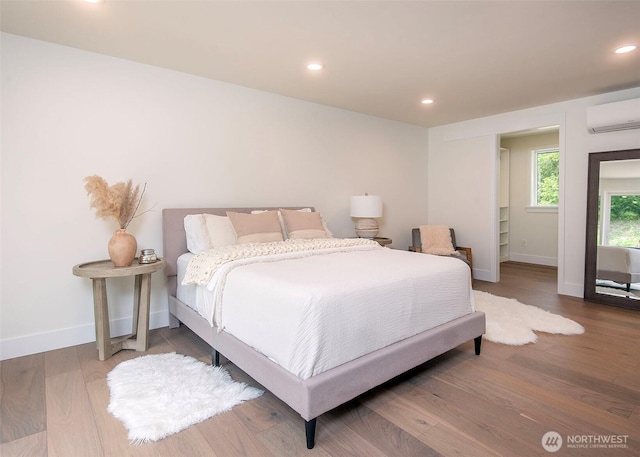 bedroom with a wall unit AC, baseboards, wood finished floors, and recessed lighting