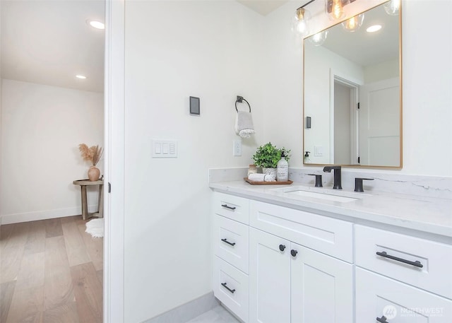 bathroom featuring vanity, baseboards, wood finished floors, and recessed lighting
