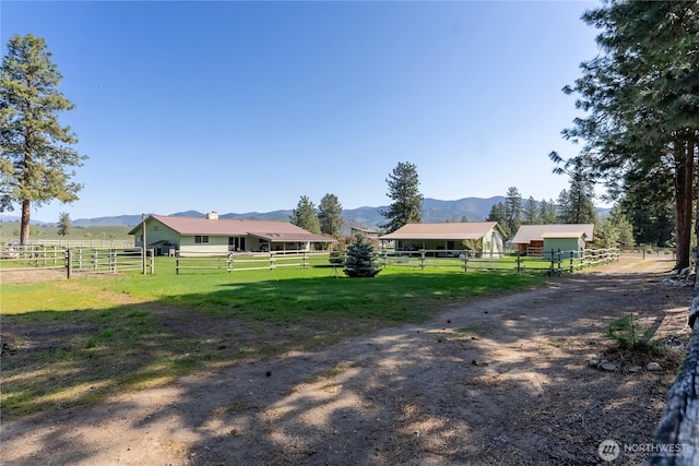 view of grassy yard with a mountain view, a rural view, an outbuilding, and an exterior structure