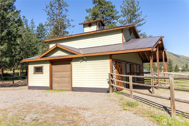 view of front of property featuring metal roof, a detached garage, an exterior structure, a mountain view, and driveway