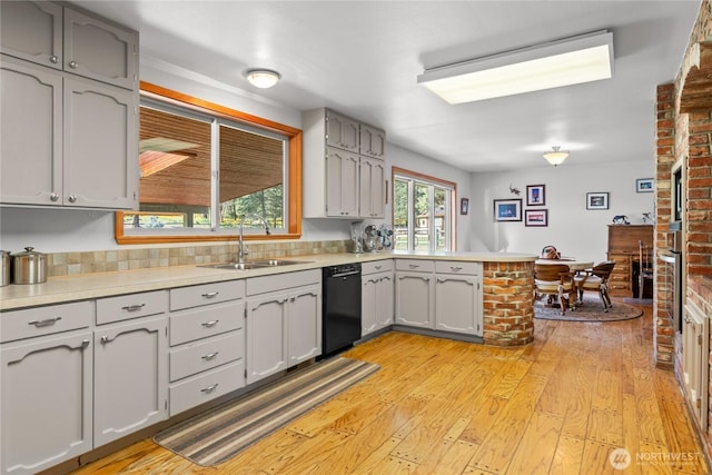 kitchen featuring dishwasher, a sink, a peninsula, light wood-style floors, and light countertops