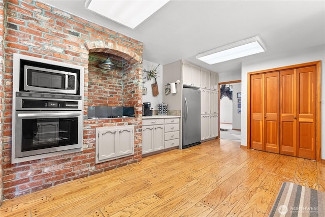 kitchen with stainless steel appliances, light wood finished floors, white cabinets, and light countertops