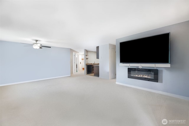 unfurnished living room featuring light carpet, baseboards, ceiling fan, and a glass covered fireplace