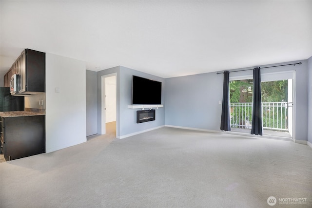 unfurnished living room featuring light carpet, a glass covered fireplace, and baseboards